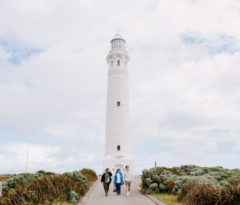 Three people walking in front of Cape Leeuwin Lighthouse