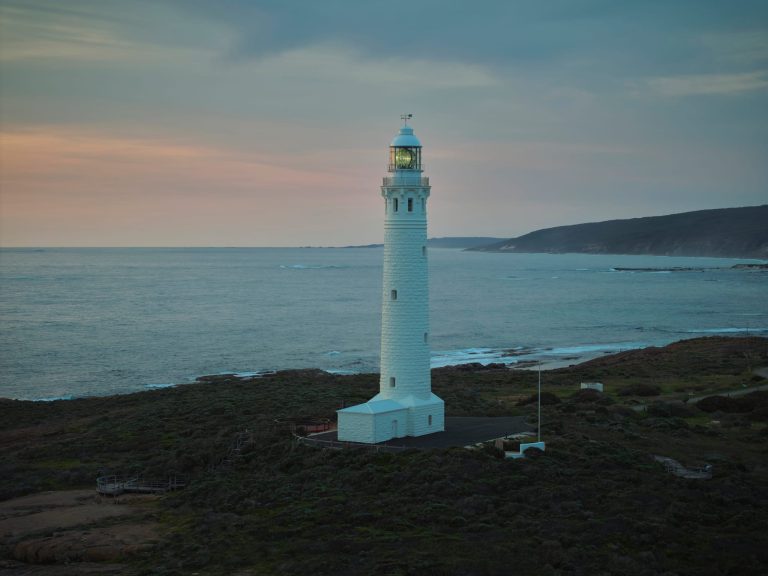 Cape Leeuwin Lighthouse glowing at sunset, casting its beam over the rugged coastline and sparkling ocean.