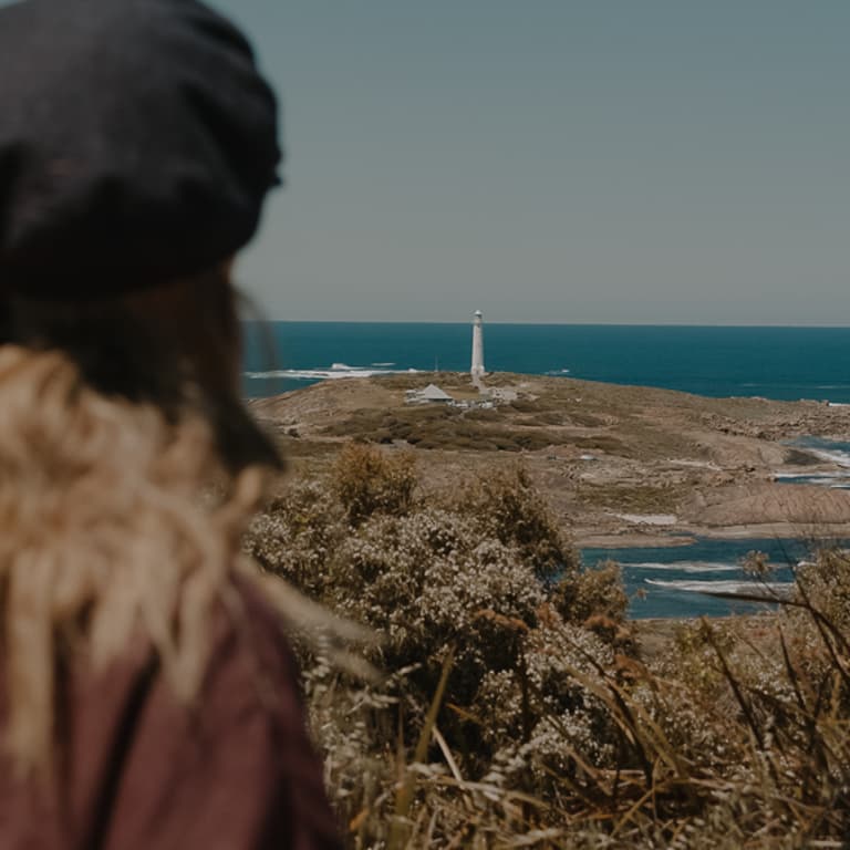The back of a woman taking in a far away view of Cape Leeuwin lighthouse from the top of the ridge.