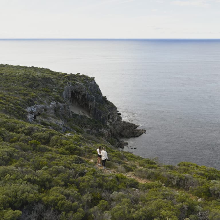 drone shot of two women on the path along Cape Naturaliste Lighthouse taking in ocean views over a cliff.