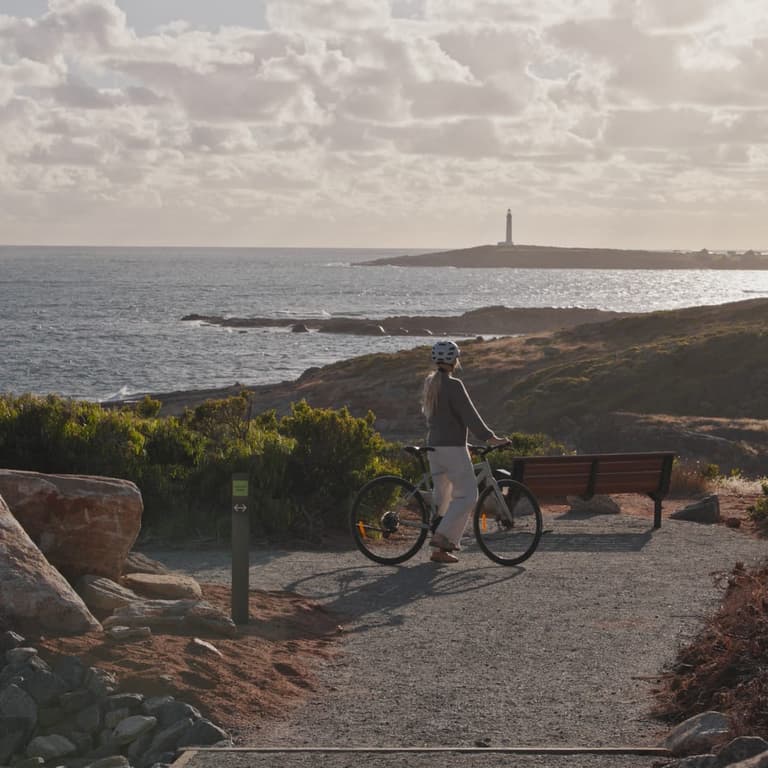 Along the Leeuwin-Biddi Trail, a bike rider pauses to admire the view of the coastline and the Cape Leeuwin Lighthouse