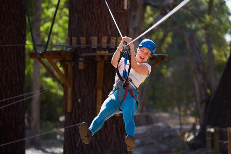 Person in a helmet and harness ziplining through the trees at Forest Adventures